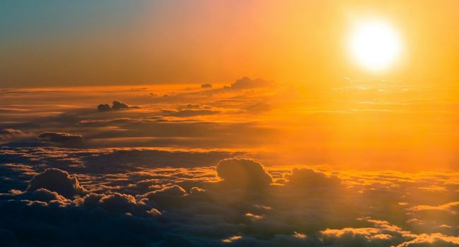 Golden sun above puffy clouds glowing in golden light.